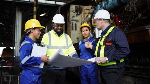 Engineers in discussion in machine maintenance in factory. Group of Industrial Engineers with Blueprint against trains and machineries industry background.
