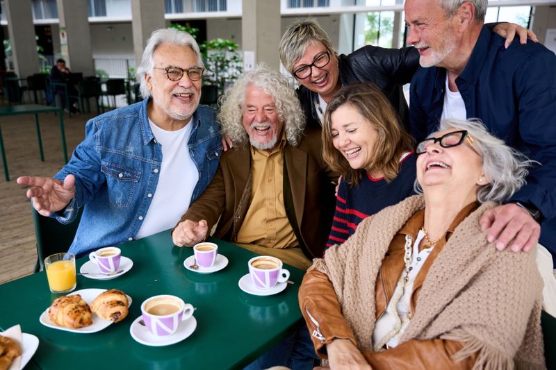 Cheerful group of mature people laughing sitting at cafeteria bar table